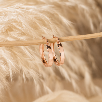 Rose gold hoop earrings on a wooden stick with a soft, blurred background