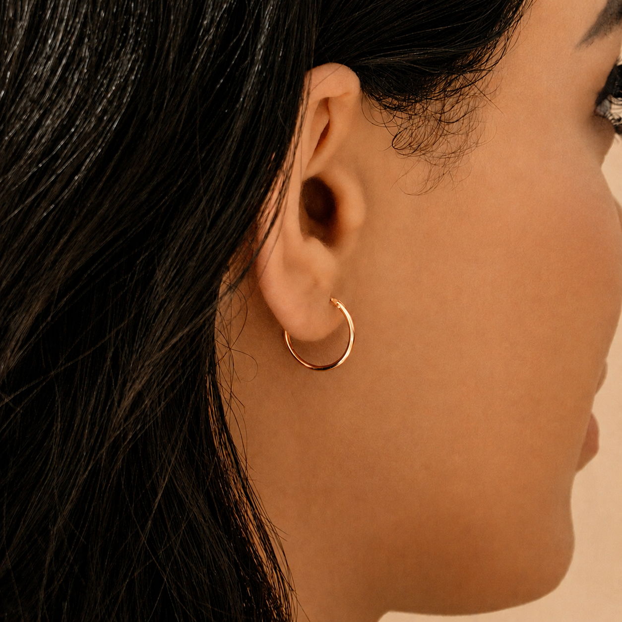 A close-up side profile of a woman wearing a delicate rose gold hoop earring.