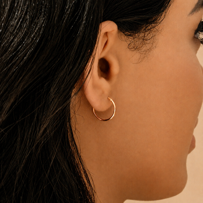 A close-up side profile of a woman wearing a delicate rose gold hoop earring.