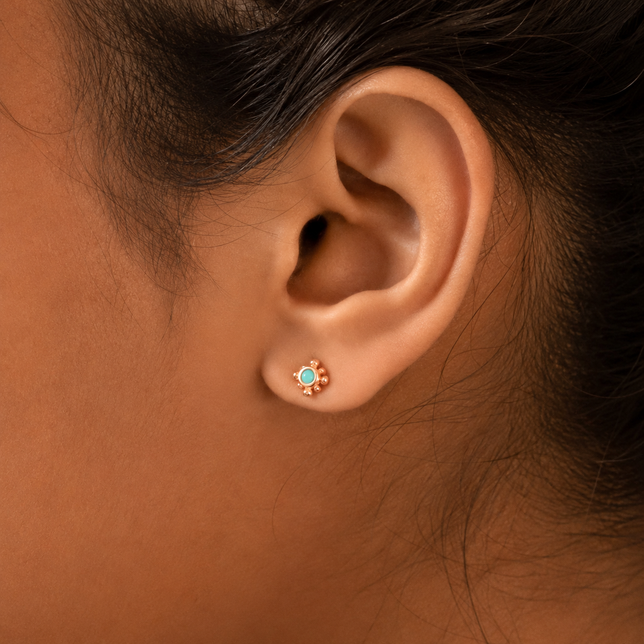 Close-up of an ear wearing a turquoise stud earring on a brown background