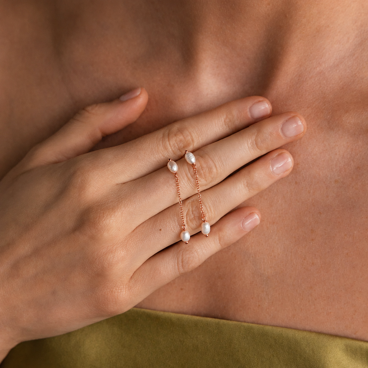 Close-up of a hand wearing a delicate pearl bracelet and ring on a neutral background