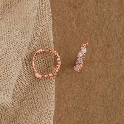 Rose gold hoop earring and small diamond earring on a textured brown surface