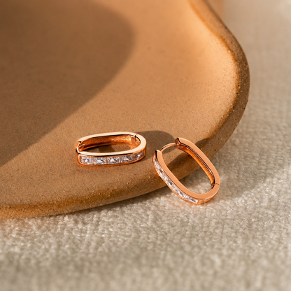 Rose gold hoop earrings on a textured beige surface