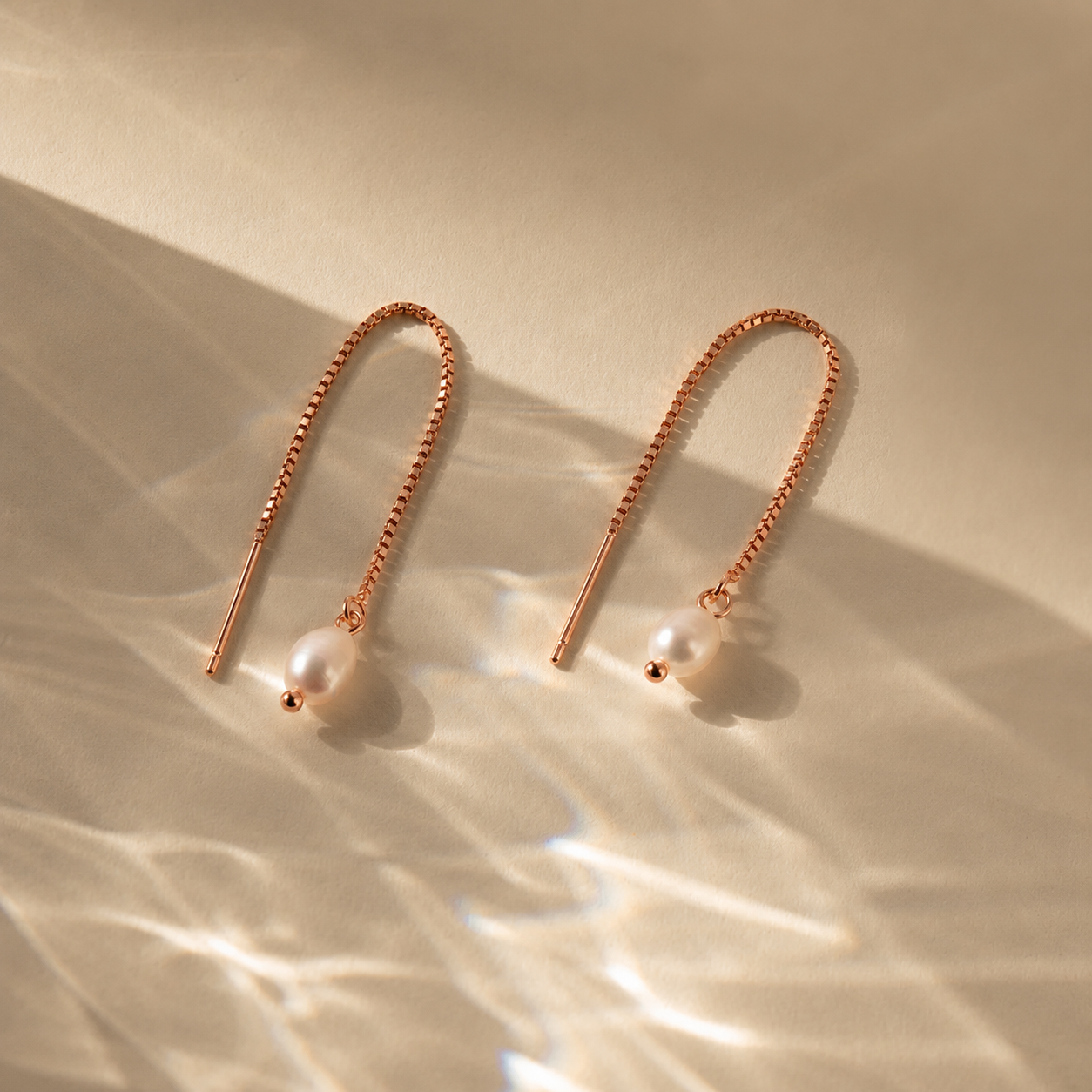 Rose gold earrings with pearl drops on a beige background