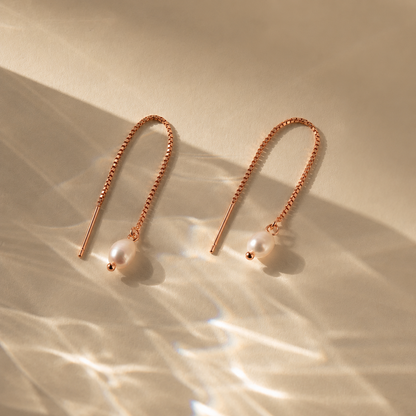Rose gold earrings with pearl drops on a beige background