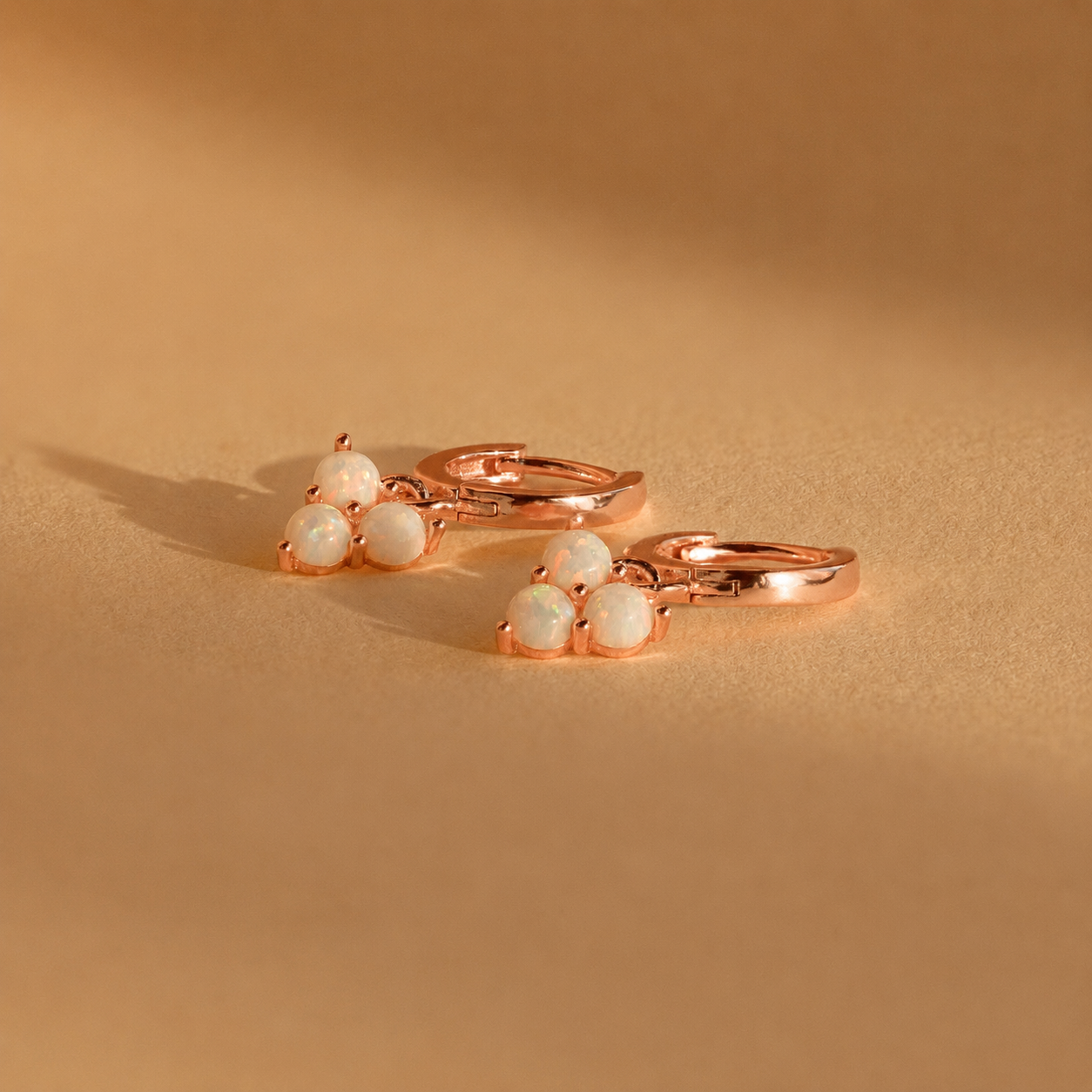 Rose gold earrings with white gemstones on a beige background