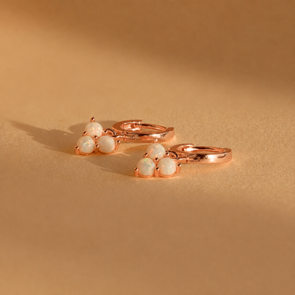 Rose gold earrings with white gemstones on a beige background