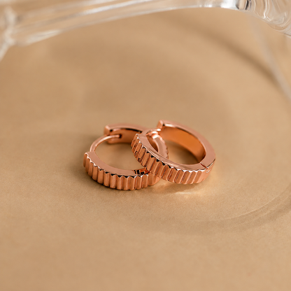 Rose gold hoop earrings on a beige surface