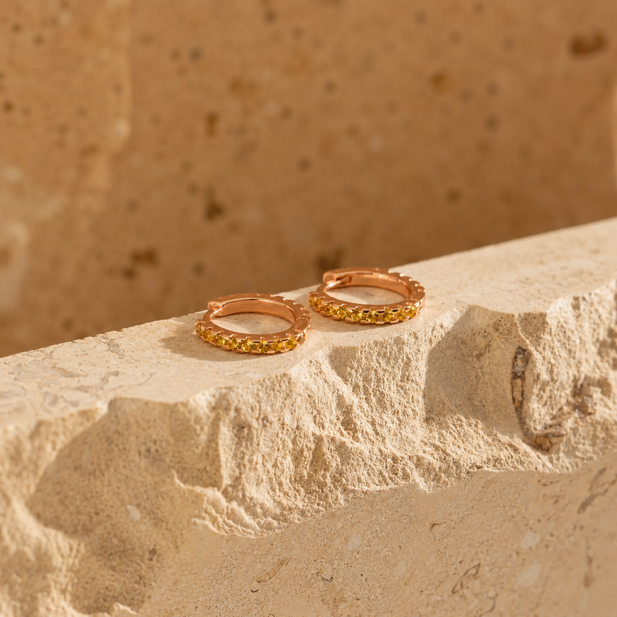 Rose gold hoop earrings with embedded stones on a textured stone surface