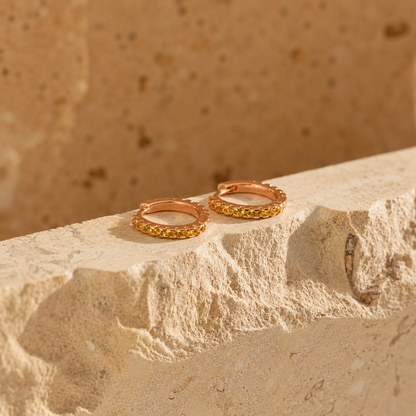 Rose gold hoop earrings with embedded stones on a textured stone surface