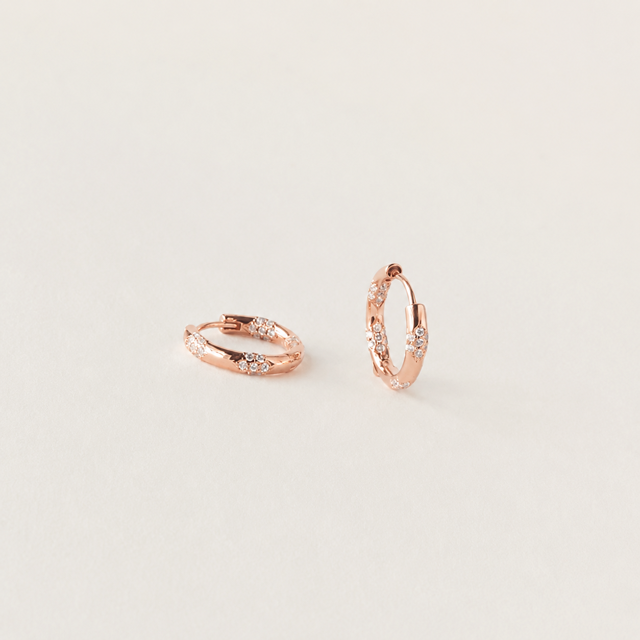 Rose gold hoop earrings with small diamonds on a light gray background