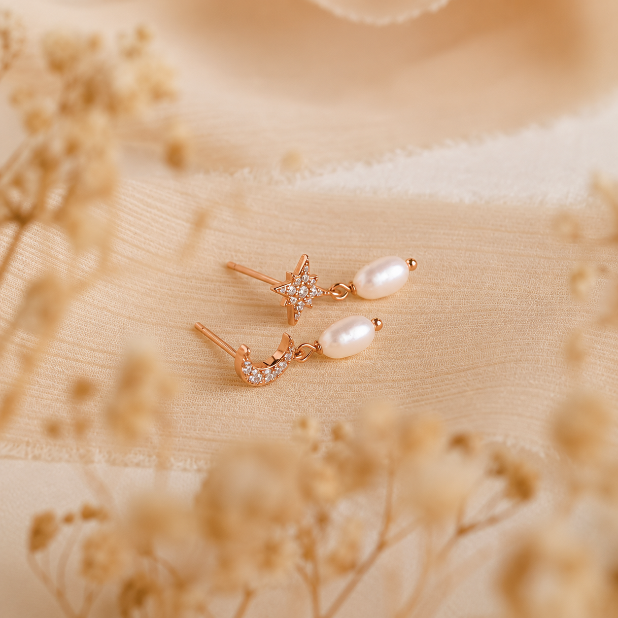 Pair of rose gold earrings with pearls on a beige fabric background