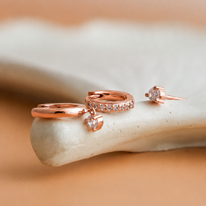 Rose gold jewelry set with rings and earrings on a stone surface