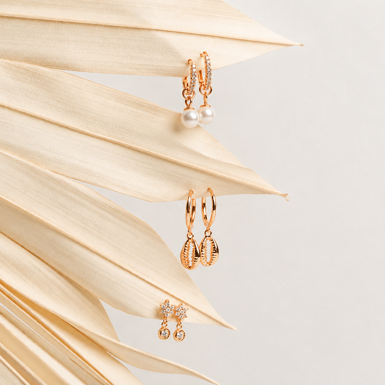 Gold earrings with pearls and gemstones on a light background with dried leaves.