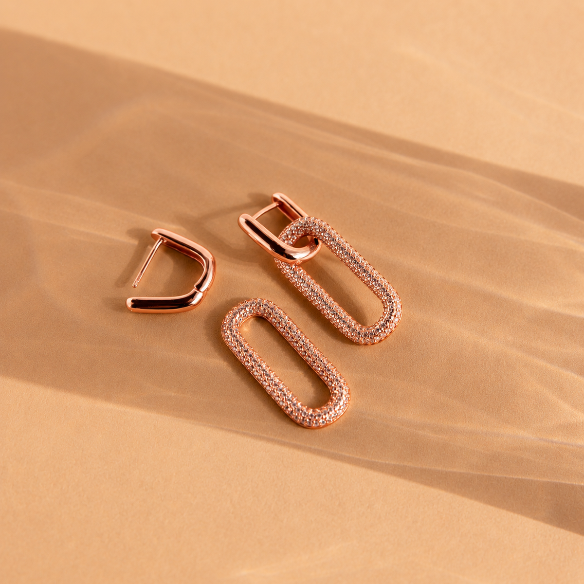 Rose gold hoop earrings on a beige sand-like background