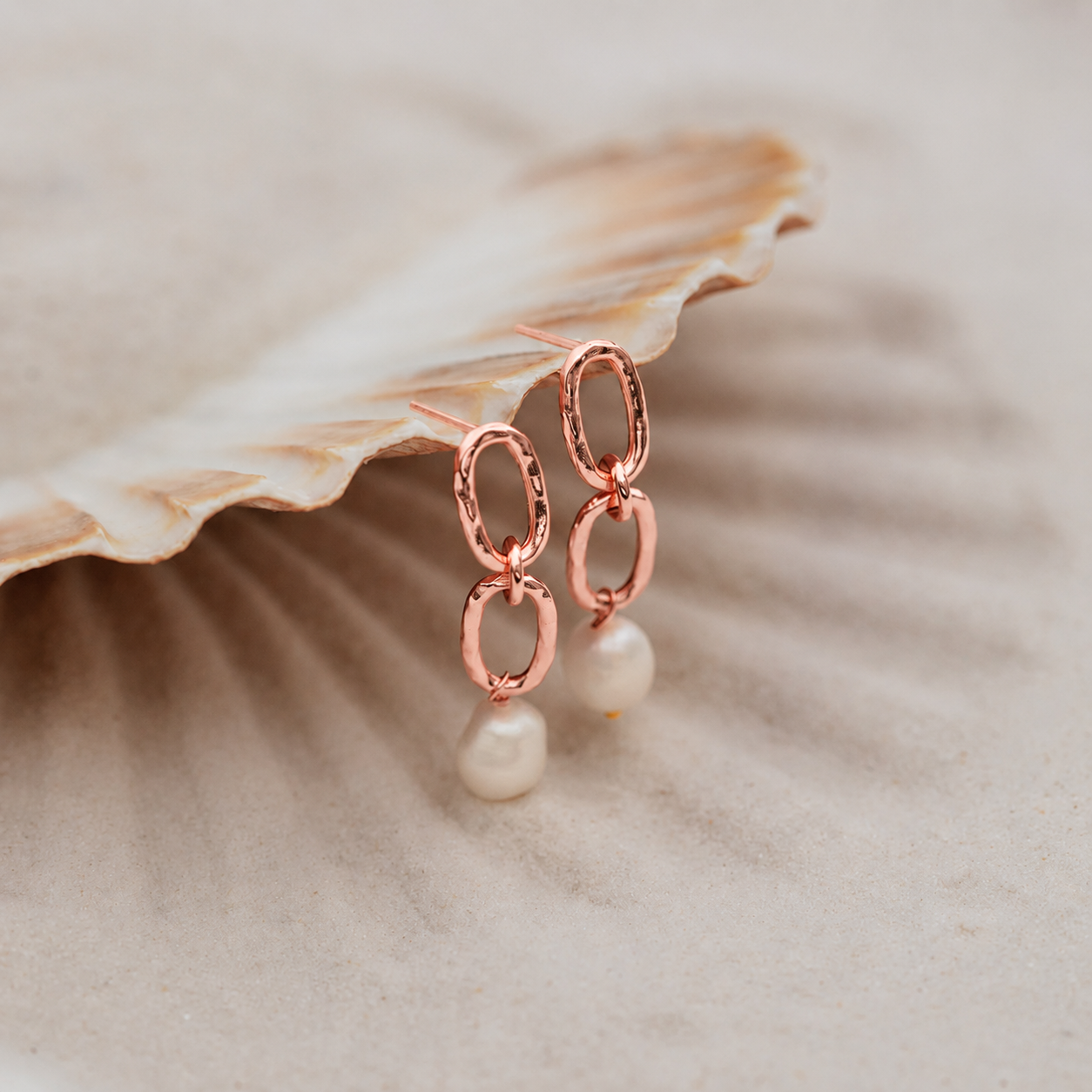 Rose gold earrings with pearls on a shell background