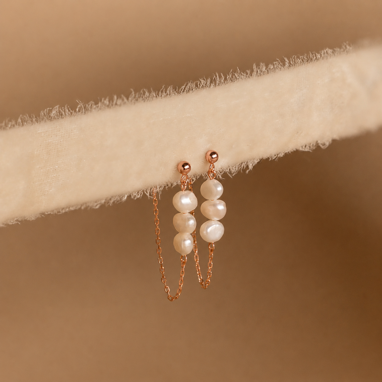 Pearl earrings with rose gold chains on a beige fabric background