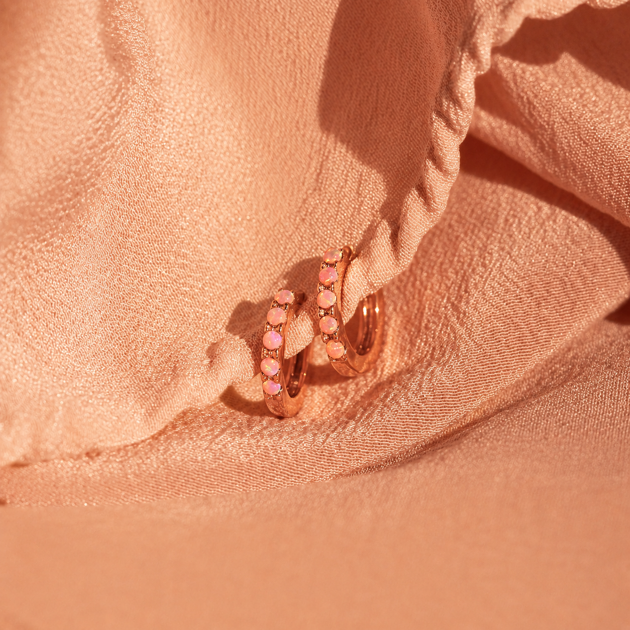 Rose gold hoop earrings with pink gemstones on a soft pink fabric background