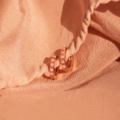 Rose gold hoop earrings with pink gemstones on a soft pink fabric background