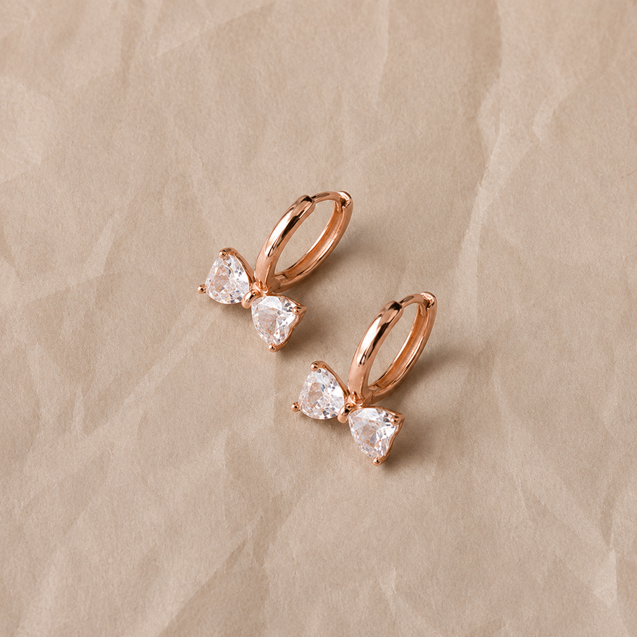 Rose gold hoop earrings with clear gemstones on a beige background
