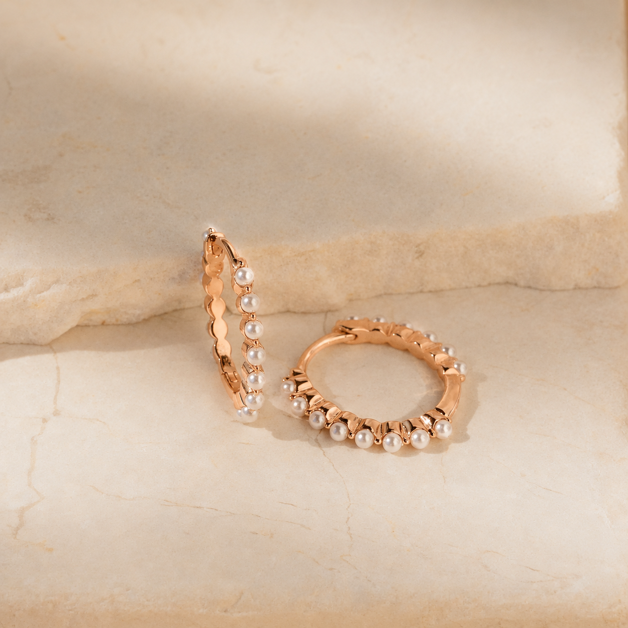 Rose gold hoop earrings with pearls on a beige stone background
