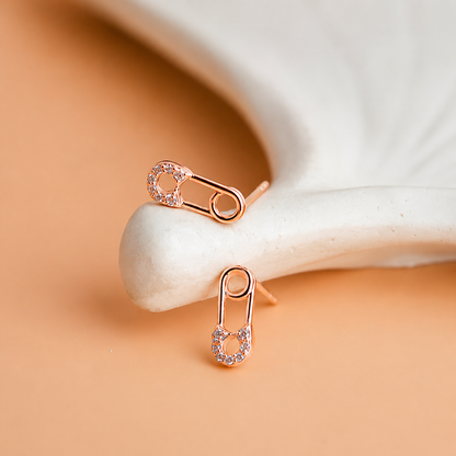 Rose gold safety pin earrings on a white stone with a beige background