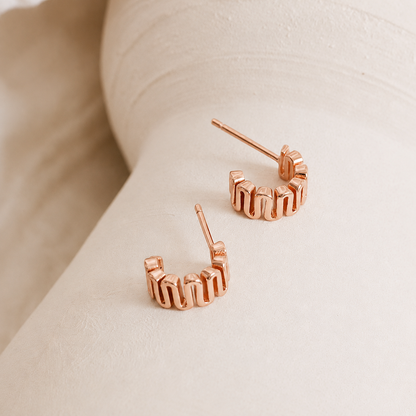 Rose gold hoop earrings on a light beige surface