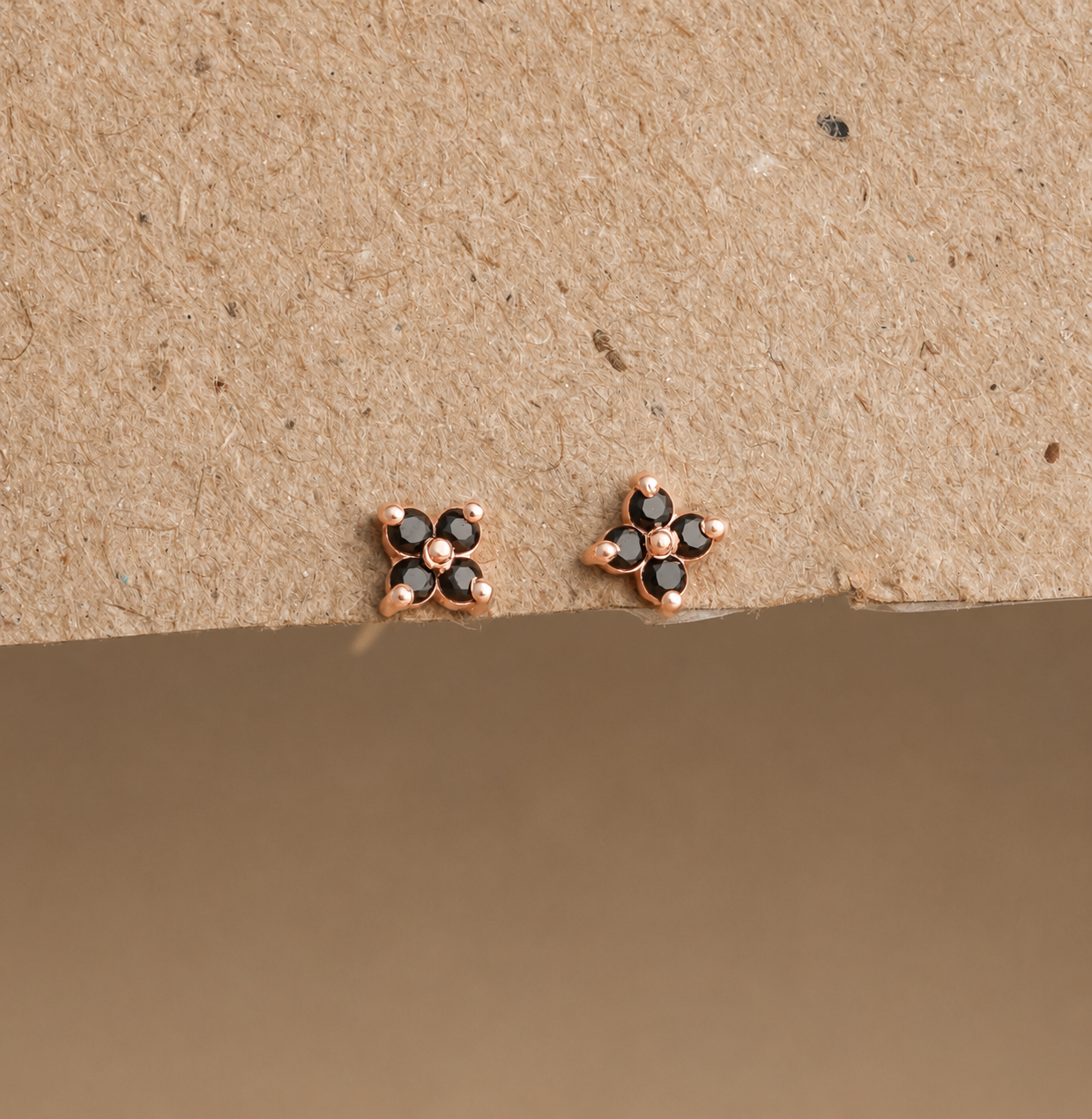 Rose gold earrings with black gemstones on a beige background