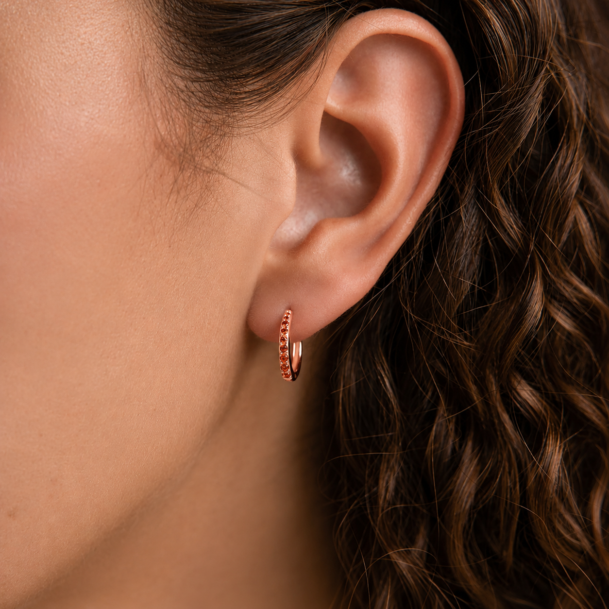 Close-up of an ear wearing a small hoop earring with a blurred background
