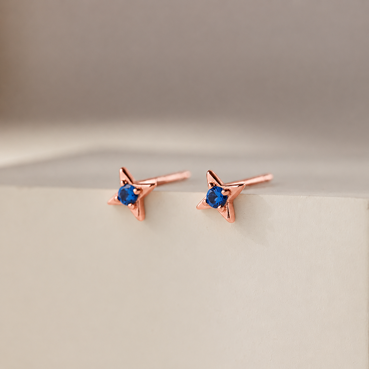 Rose gold star-shaped earrings with blue gemstones on a beige background