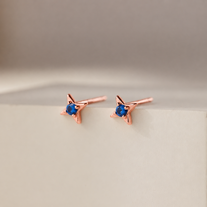 Rose gold star-shaped earrings with blue gemstones on a beige background
