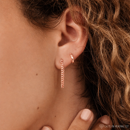 Close-up of an ear wearing rose gold hoop earrings with a blurred background.
