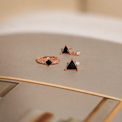 Rose gold jewelry set with black gemstones on a neutral background
