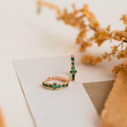 Rose gold rings with green gemstones on a white surface with dried flowers.