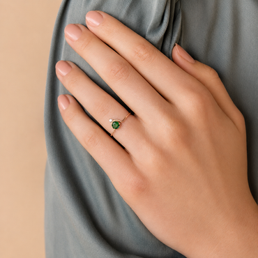 Hand wearing a green gemstone ring on a neutral background