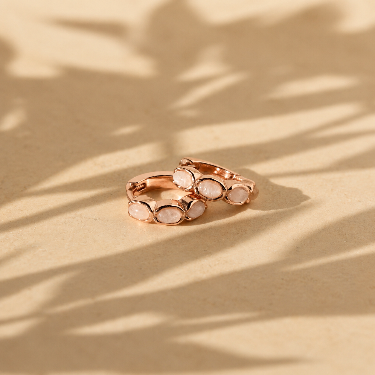 Rose gold ring with white stones on a beige surface with leaf shadows