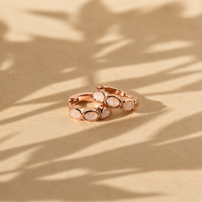 Rose gold ring with white stones on a beige surface with leaf shadows