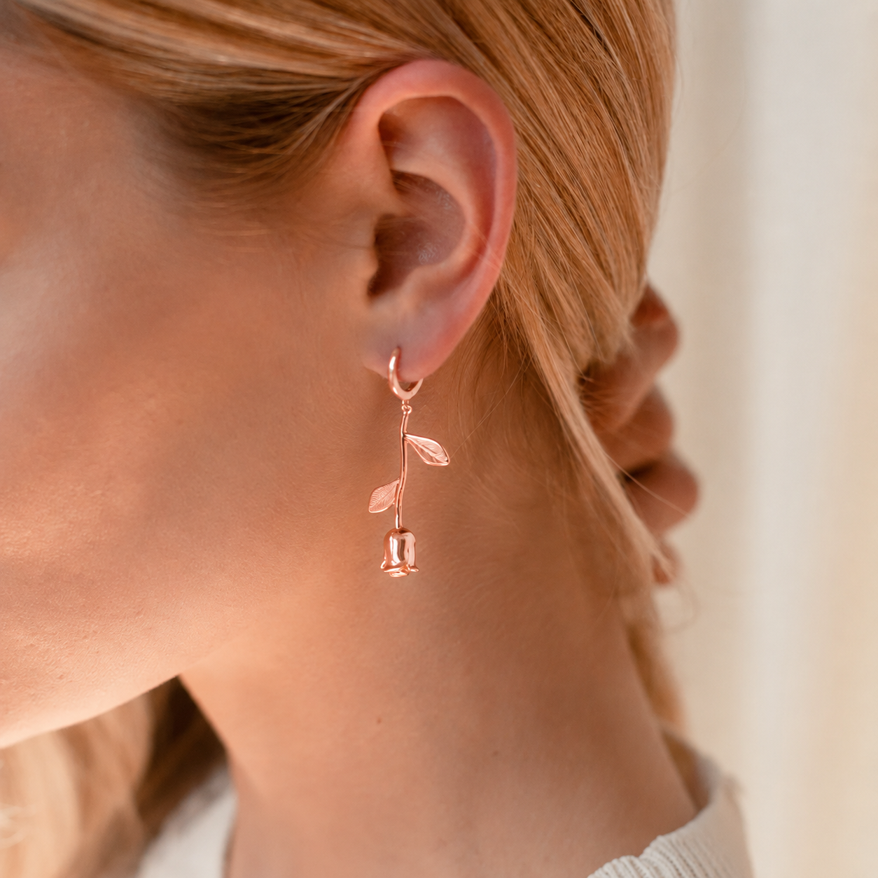 Rose gold floral earring worn by a person with a blurred background
