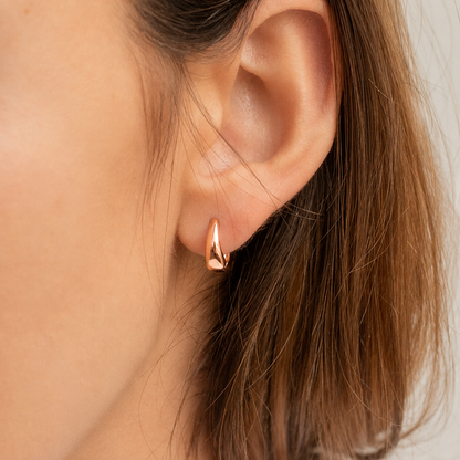 Close-up of an ear wearing a gold hoop earring with a neutral background