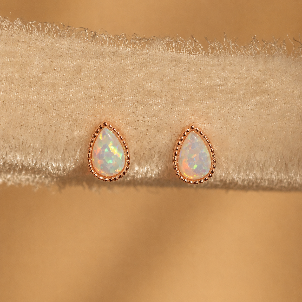 Teardrop-shaped opal earrings with rose gold setting on beige fabric background