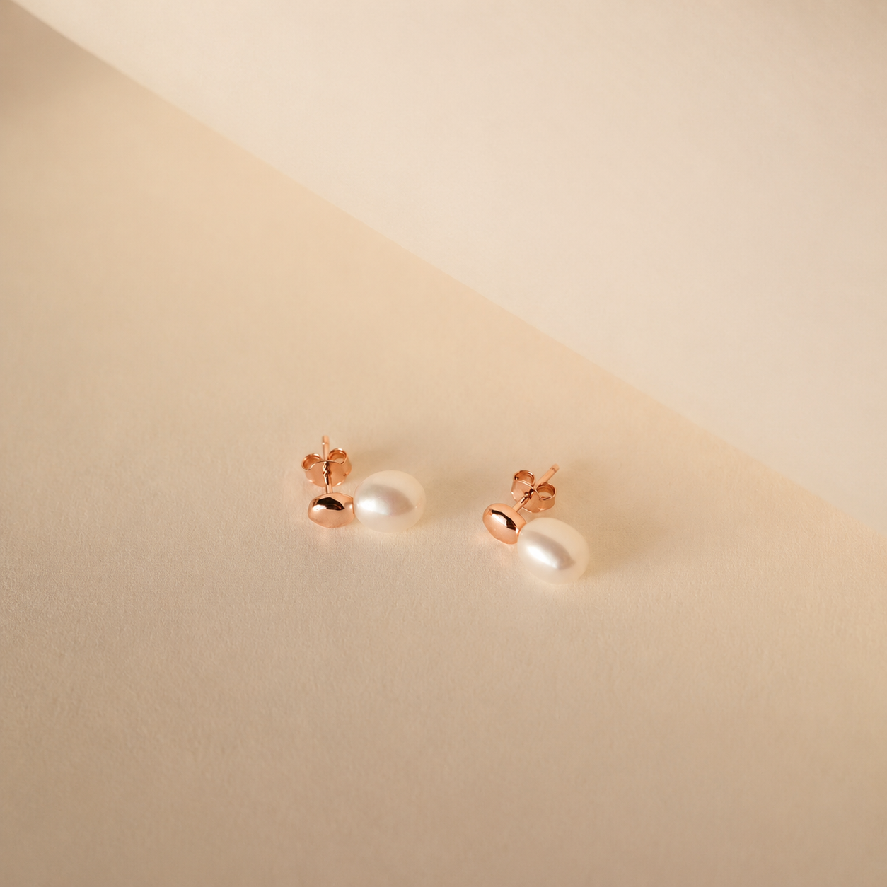 Pair of pearl earrings with rose gold posts on a beige background