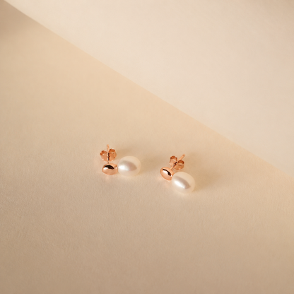 Pair of pearl earrings with rose gold posts on a beige background