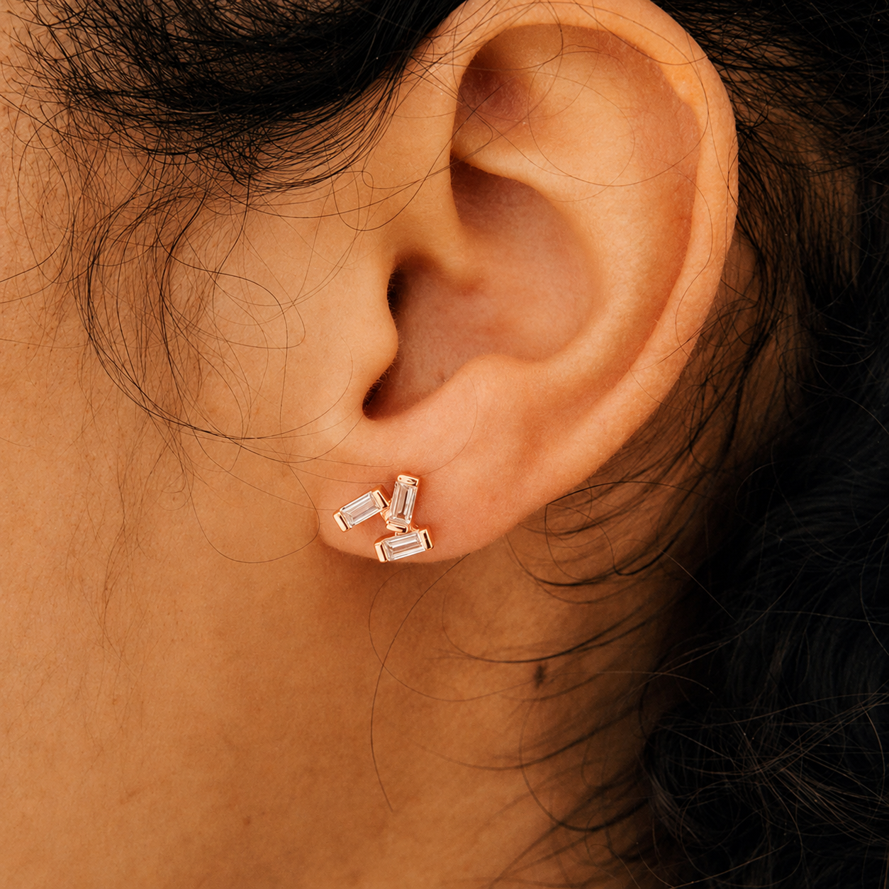 Close-up of an ear wearing gold stud earrings with a blurred background