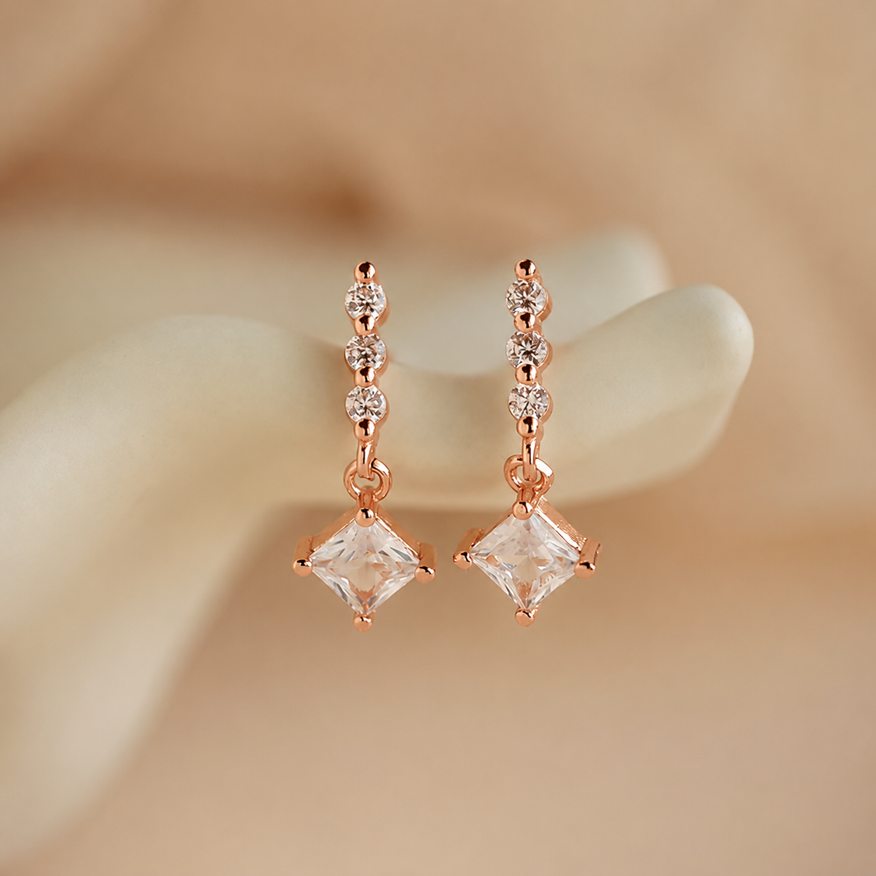 Rose gold earrings with clear gemstones on a beige background