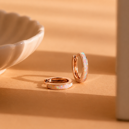 Rose gold hoop earrings with colorful enamel on a beige surface