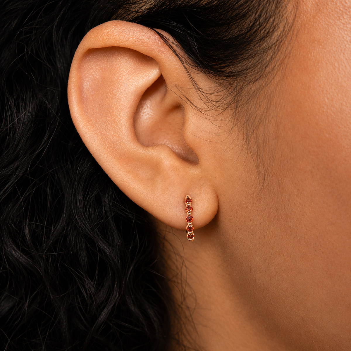 Close-up of an ear wearing a small hoop earring with red gemstones.