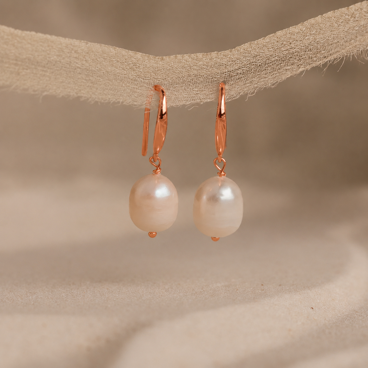 Pearl earrings with rose gold hooks on a beige fabric background