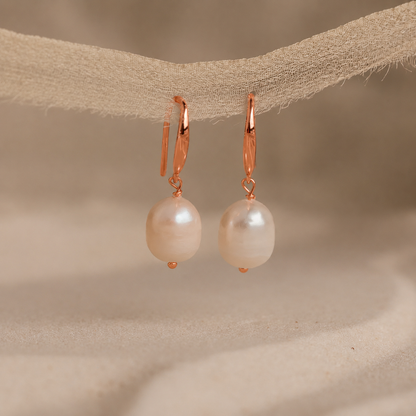 Pearl earrings with rose gold hooks on a beige fabric background