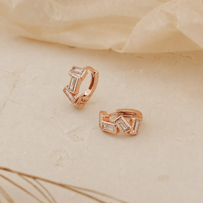Rose gold hoop earrings with clear gemstones on a beige fabric background