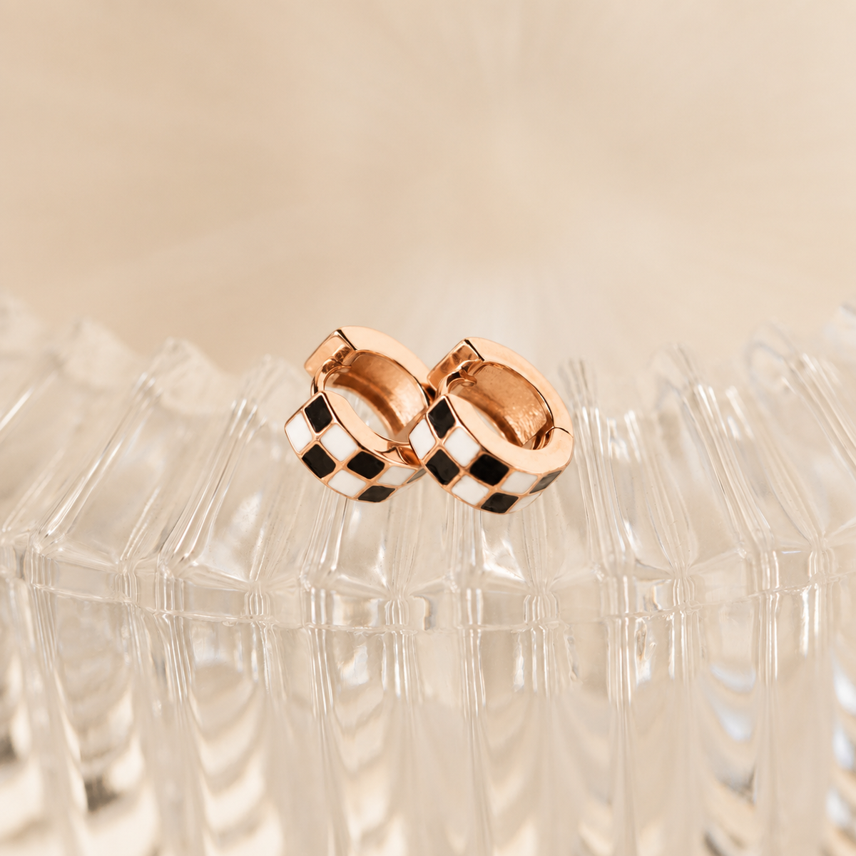 Rose gold hoop earrings with black checkered pattern on a beige background
